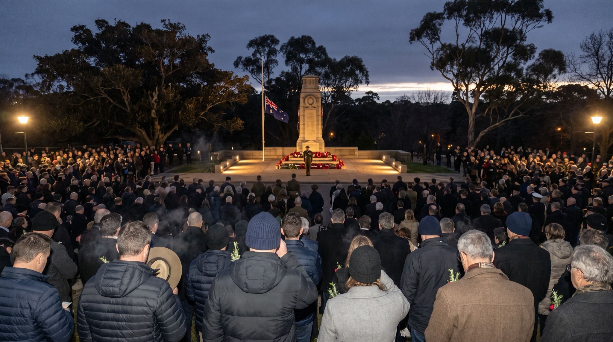 An Australian dawn service seen from behind a vast crowd in the last darkness before sunrise, thousands of heads and shoulders packed together